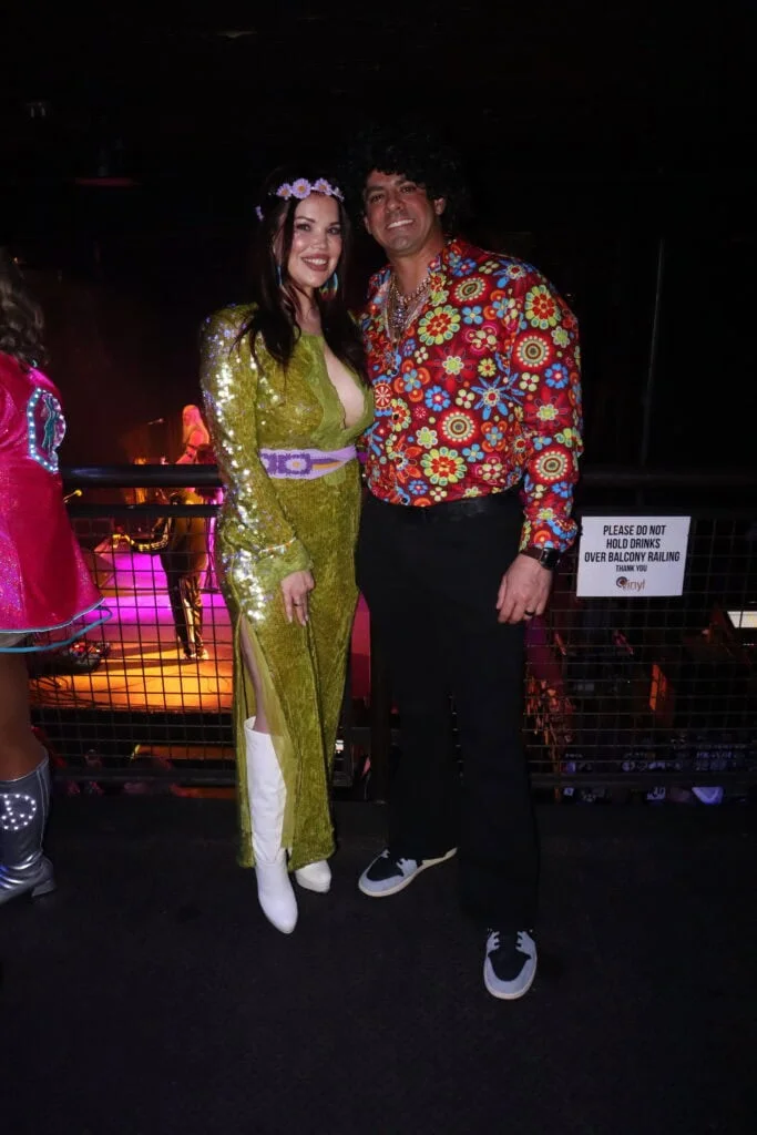Two guests in shiny gold and colorful floral outfits at the ball